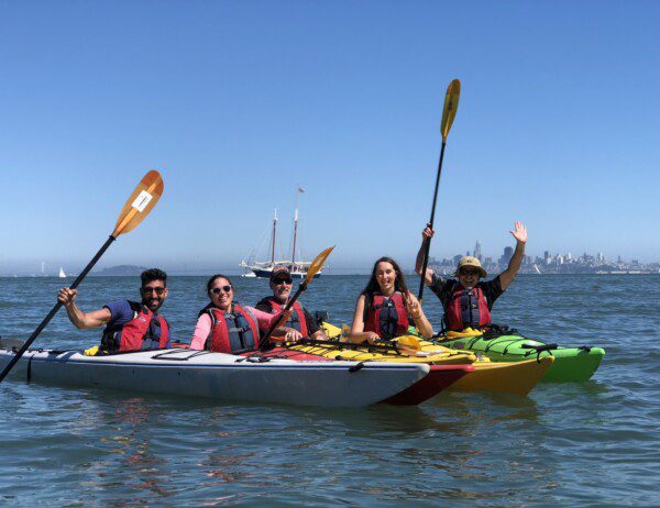 LGBTQ+ group of kayakers on a community paddle & tour with San Francisco as the backdrop in the distance.